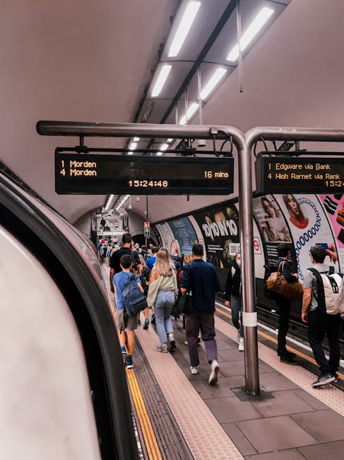 Inside a busy underground train station in High Barnet, a crowd of passengers is seen on the platform preparing for departure. The individuals are dressed in casual and business attire, carrying backp