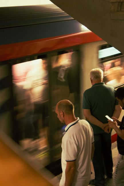 Inside a busy underground train station in High Barnet, a crowd of passengers is seen on the platform preparing for departure. The individuals are dressed in casual and business attire, carrying backp
